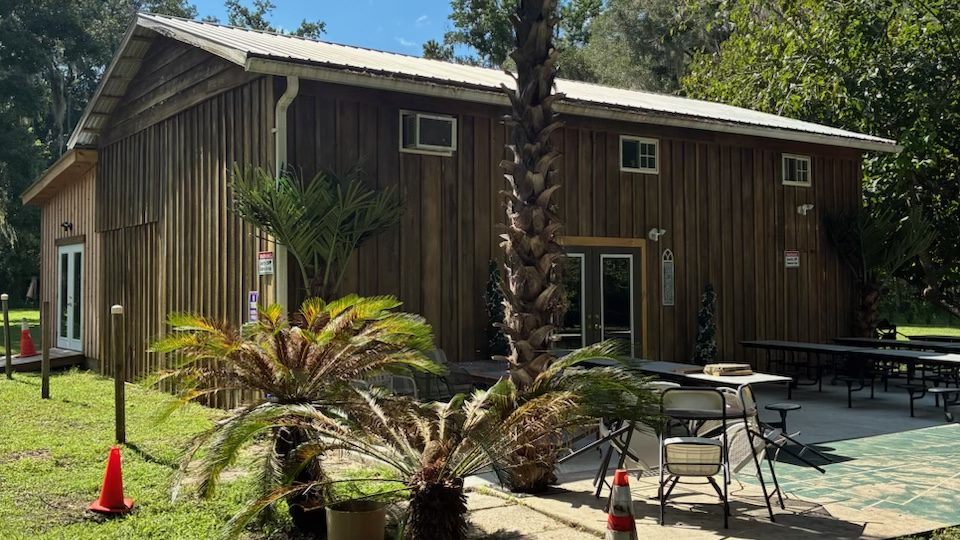 A timber barn with a covered patio, picnic tables and palms, on the club's farm.
